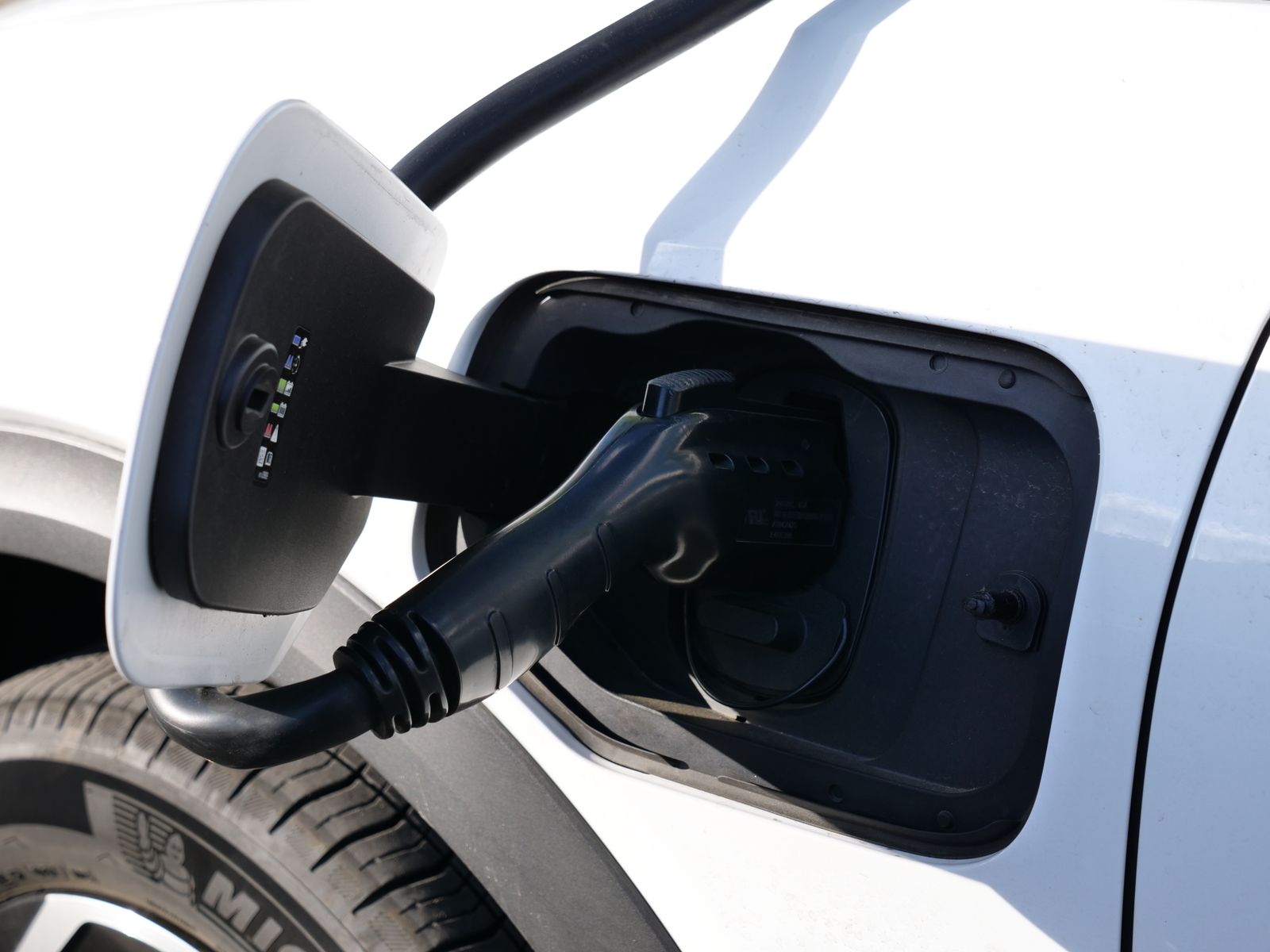 Voiture électrique branchée sur une borne, capot ouvert avec technicien en arrière-plan